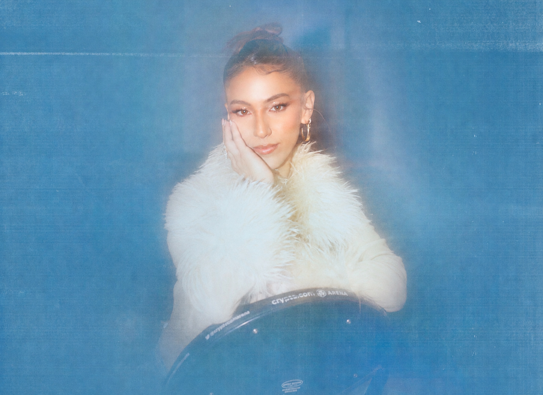 Yari M in a white feathered jacket against a dreamy blue backdrop